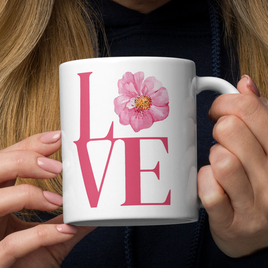 Woman holding a white mug with 'LOVE' and a pink flower design.